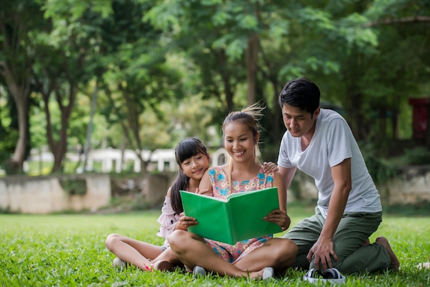 Família feliz mãe, pai e filha ler um livro no parque