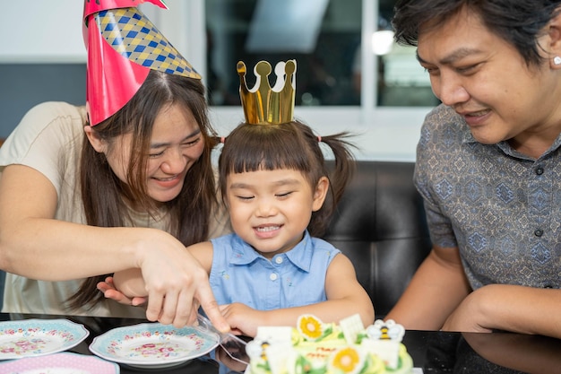 Família feliz se divertindo na festa de aniversário criança comemorando aniversário e cortando bolo para compartilhar