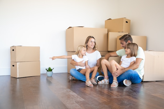 Família feliz sentada no chão em uma nova casa perto de caixas de papelão