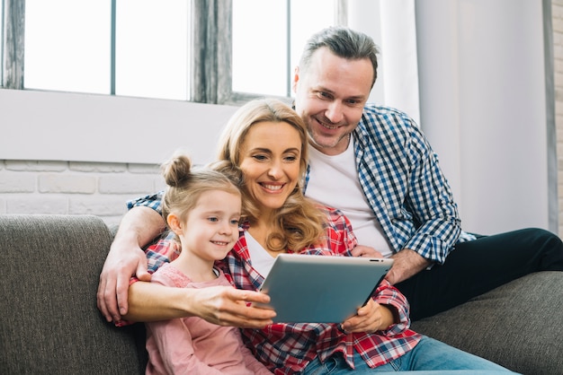 Família feliz usando tablet digital no sofá na sala de estar