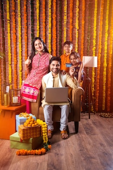Família indiana jovem asiática comprando online na noite do festival de diwali com cartão eletrônico e laptop