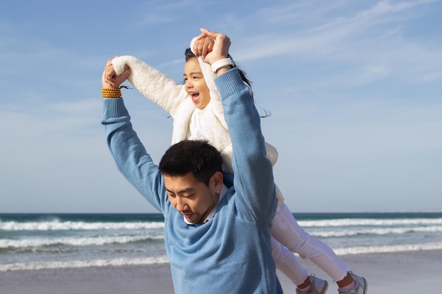 Família japonesa feliz passando tempo na praia. Pai e filha brincando, rindo, cavalgando, brincando. Lazer, tempo para a família, conceito de parentalidade