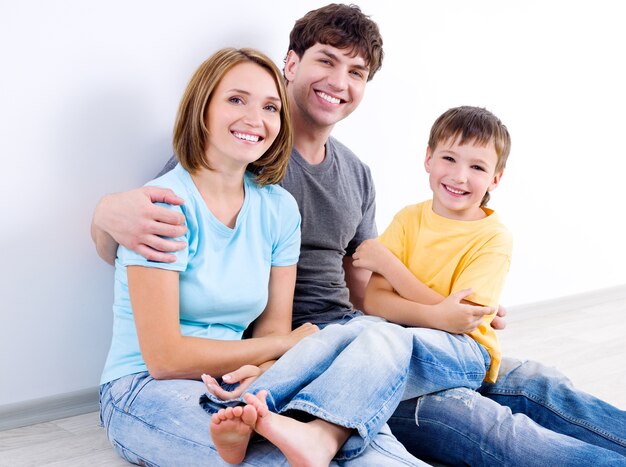 Família jovem bonita e feliz em roupas casuais, sentada no chão - dentro de casa