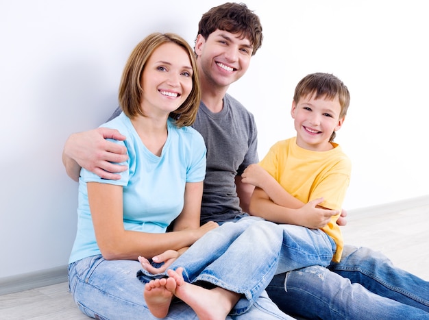 Família jovem bonita e feliz em roupas casuais, sentada no chão - dentro de casa