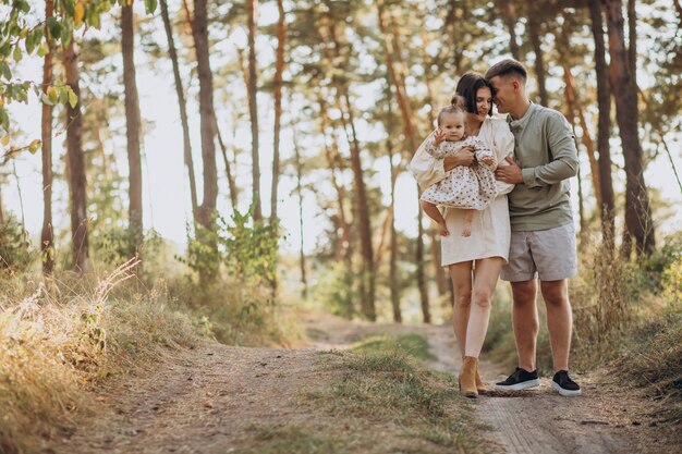 Família jovem com filha pequena caminhando na floresta ao pôr do sol