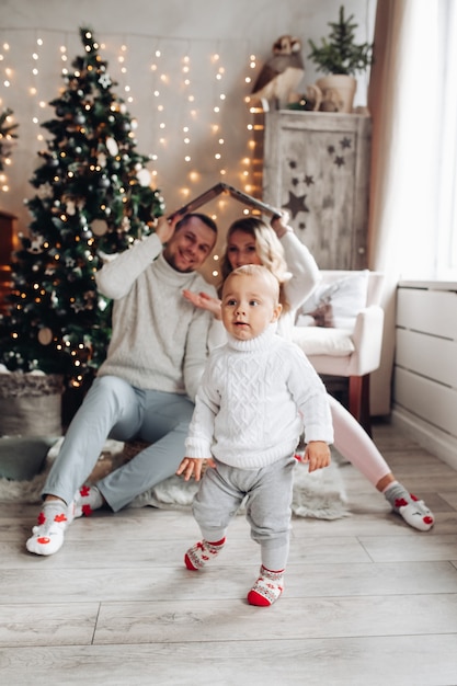 Família jovem com uma criança na sala decorada com árvore de natal