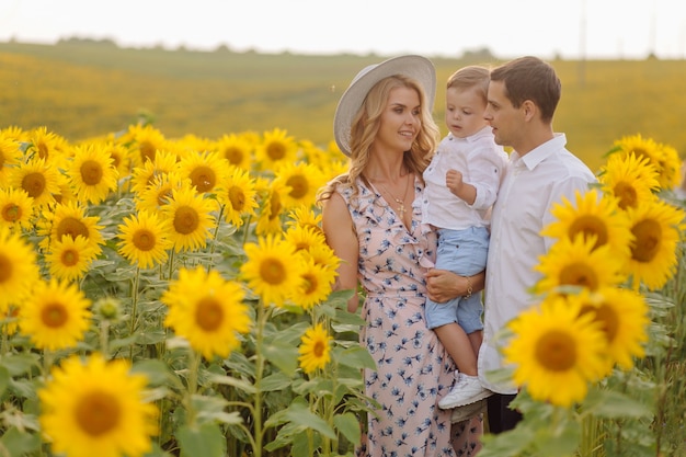 Família jovem feliz, pai mãe e filho, estão sorrindo, segurando e abraçando no campo de girassol