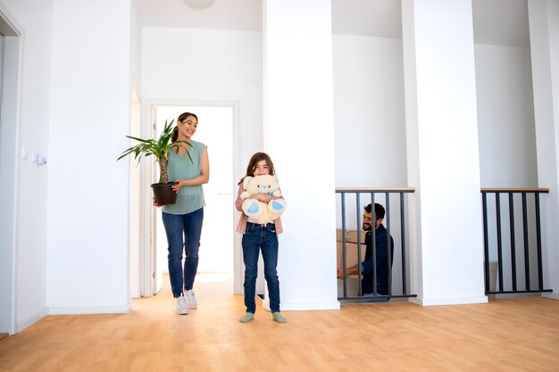 Família jovem se mudando para um novo apartamento carregando flores e caixas com pertences.