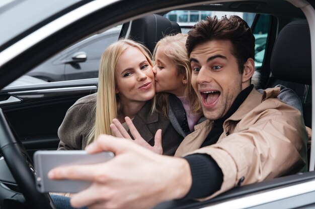 Família jovem sorridente faz selfie pelo telefone móvel.