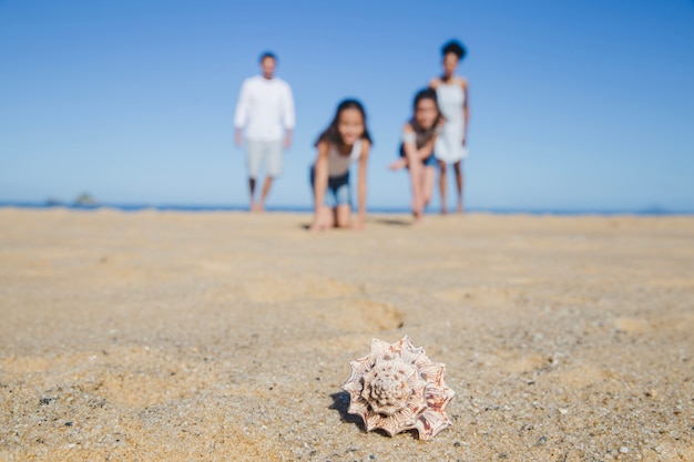 Família na praia com concha no primeiro plano