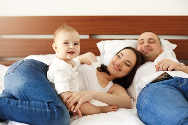 Família nova feliz do pai da mãe e alegria pequena de sorriso da mulher do bebê que encontra-se na cama em casa. concentre-se na filha.