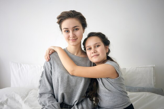 Família perfeita. Retrato de uma linda garota de 12 anos com longos cabelos escuros, sentada na cama