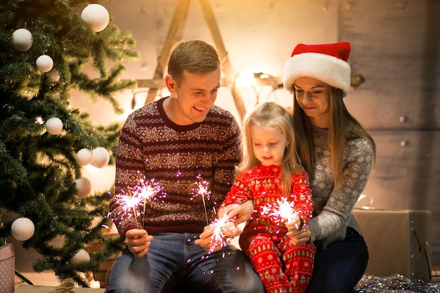 Família sentada pela árvore de natal com luzes de bengala