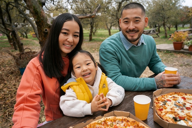 Família sorridente de tiro médio comendo pizza ao ar livre