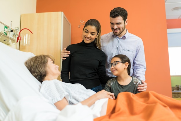 Família sorridente visitando mulher sênior durante o tratamento no hospital