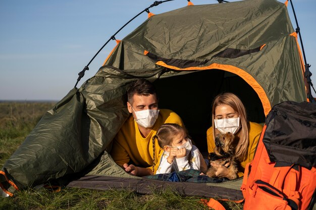 Família usando máscaras e sentada na barraca com a vista frontal do cachorro