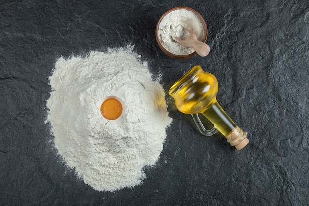 Farinha com gema de ovo e frasco de óleo em superfície escura.