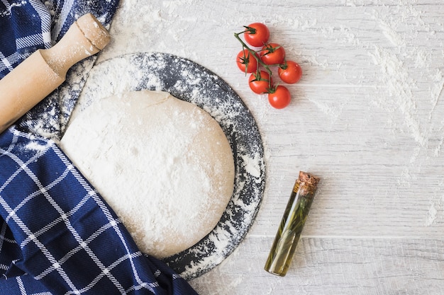 Foto grátis farinha polvilhada com pão de massa; tomate cereja; alecrim e rolling pins na prancha de madeira