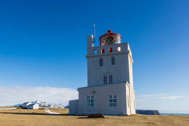 Farol em Dyrholaey sob a luz do sol e um céu azul na Islândia