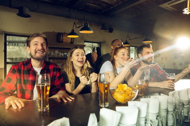 Fãs de esportes torcendo em um bar e bebendo cerveja durante a competição do campeonato