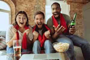 Foto grátis fãs de futebol animados assistindo jogo de esporte em casa, suporte remoto do time favorito durante surto de pandemia de coronavírus