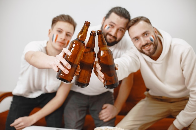 Fãs de futebol sentados no sofá da sala bebendo cerveja
