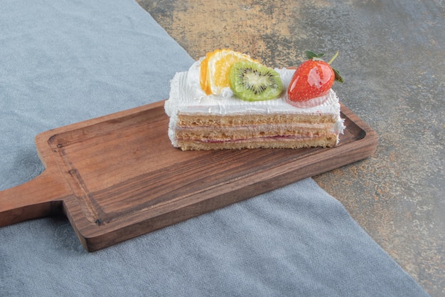 Foto grátis fatia de bolo com cobertura de frutas e creme em uma pequena placa de madeira