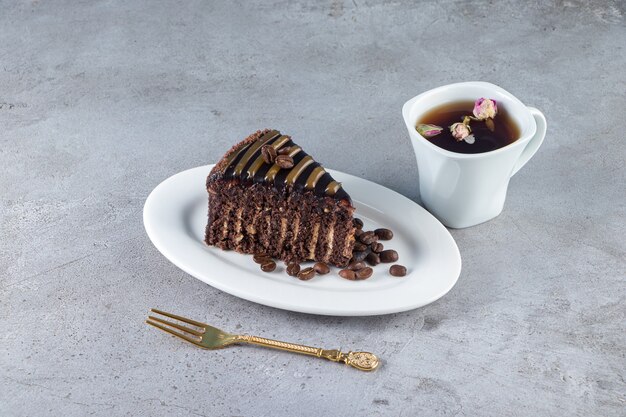 Fatia de bolo de chocolate e copo de chá na mesa de pedra.