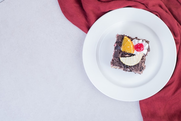 Fatia de bolo de chocolate na chapa branca com toalha de mesa vermelha.