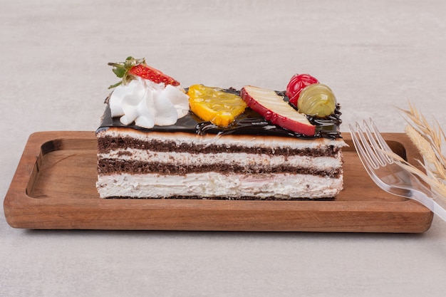 Fatia de bolo de chocolate na placa de madeira com fatias de frutas.