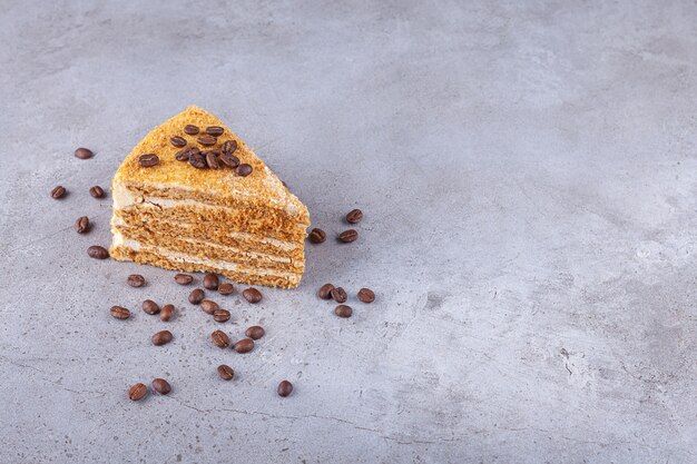 Fatia de bolo de mel em camadas com grãos de café colocados sobre um fundo de pedra.