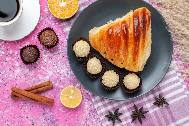 Fatia de pastelaria vista de perto superior com canela e bombons de chocolate no fundo rosa.