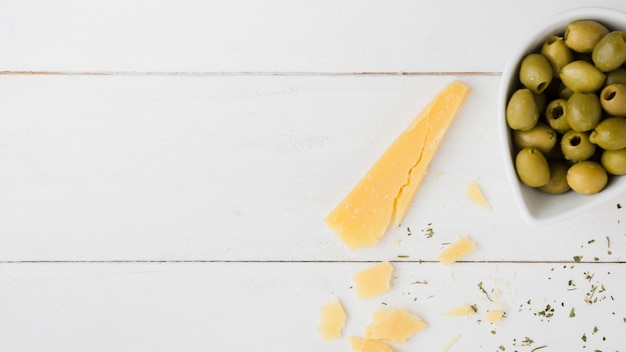 Fatia de queijo com azeitonas verdes na tigela na mesa de madeira branca