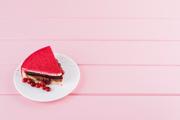 Fatia deliciosa do bolo com bagas da passa de Corinto vermelha na placa branca sobre o contexto da prancha cor-de-rosa