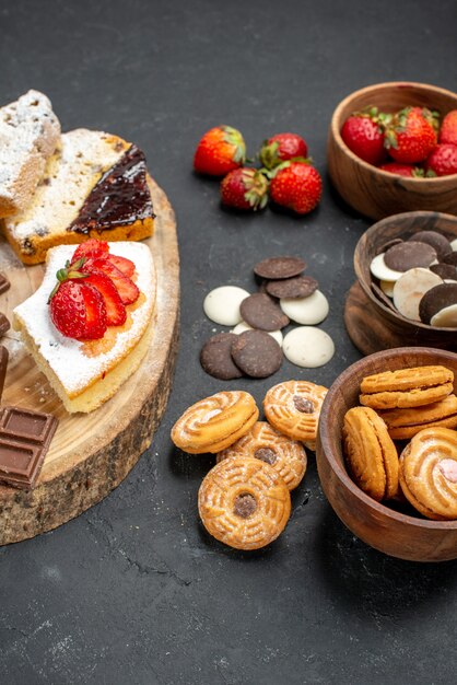 Fatias de bolo de frente com barras de chocolate e biscoitos em fundo cinza