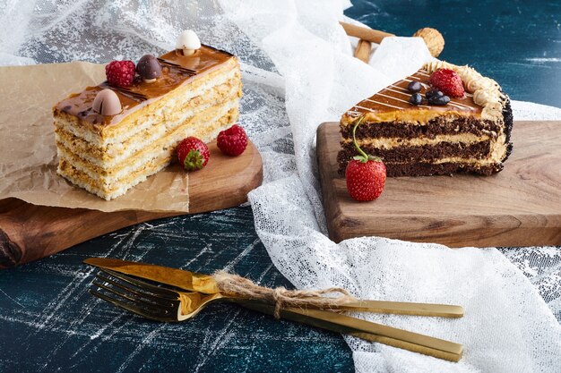 Fatias de bolo na placa de madeira com frutas ao redor.