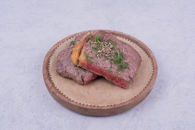 Fatias de carne de bife com ervas e especiarias em uma placa de madeira.
