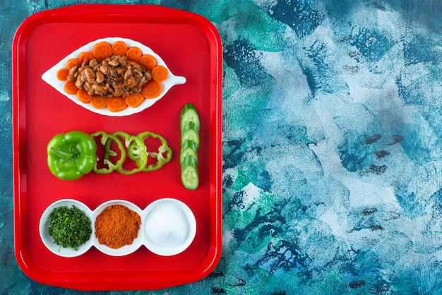 Fatias de cenoura, feijão e legumes em um prato em uma bandeja, na mesa azul.