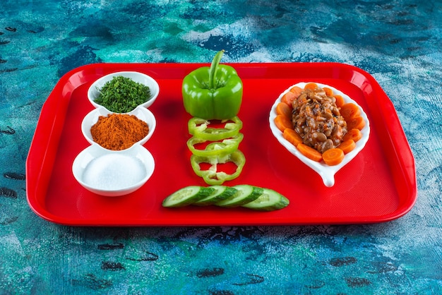 Fatias de cenoura, feijão e legumes em um prato em uma bandeja, na mesa azul.