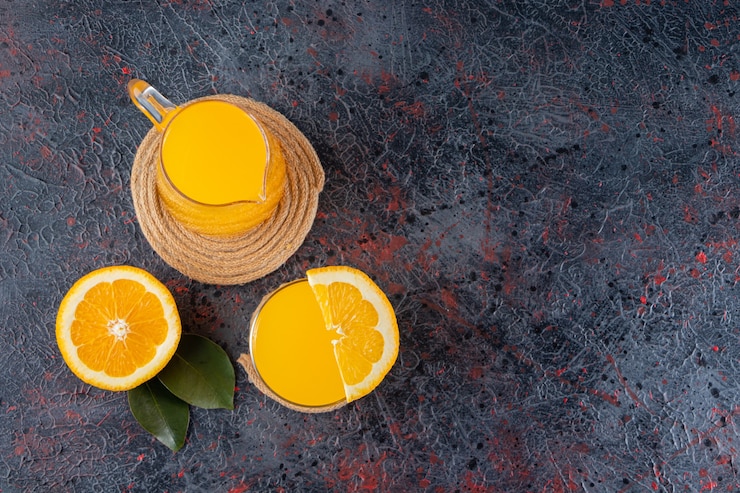 Foto grátis fatias de frutas frescas de laranja com folhas e uma jarra de vidro com suco colocado na mesa de pedra.