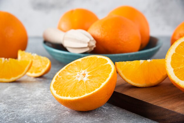 Fatias de frutas laranja com laranjas inteiras em uma placa de madeira.
