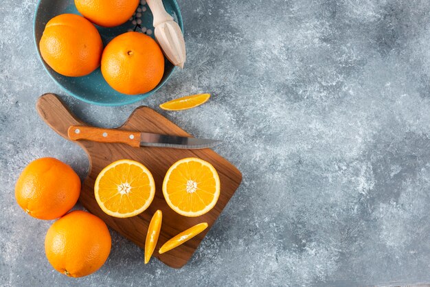 Fatias de frutas laranja com laranjas inteiras em uma placa de madeira.