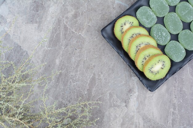 Fatias de kiwi e doces de geleia na placa preta.