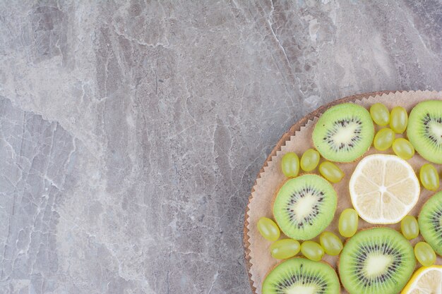 Fatias de kiwi, uvas e limão na placa de madeira.