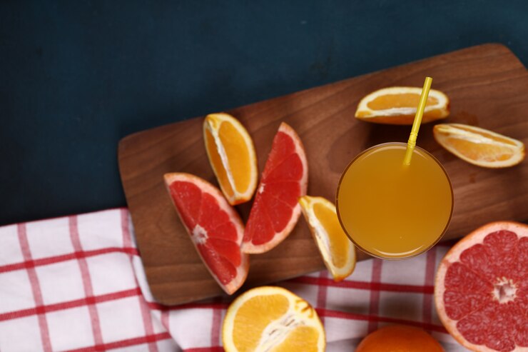 Foto grátis fatias de laranja e toranja com um copo de bebida na placa de madeira. vista do topo.