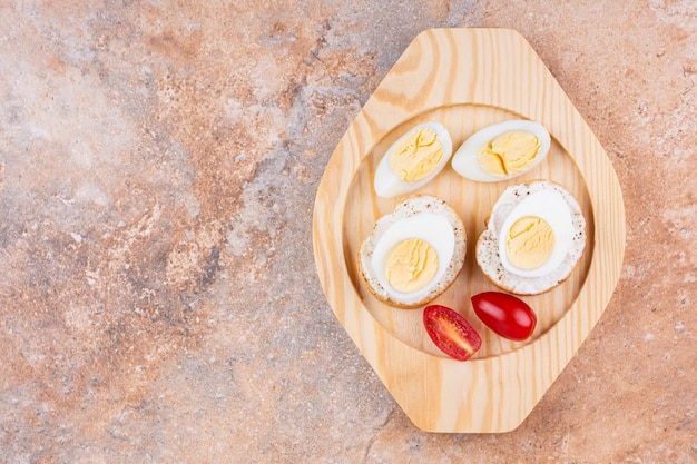 Fatias de ovo cozido, tomate e pão baguete em uma placa de madeira, no fundo de mármore.