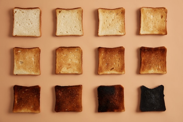 Fatias de pão de vários graus de tostado dispostas em fileiras contra um fundo bege. Torrada ou lanche para comer. Estágios de tostagem. Conceito de alimentação, larica e dieta saudável. Foto de estúdio