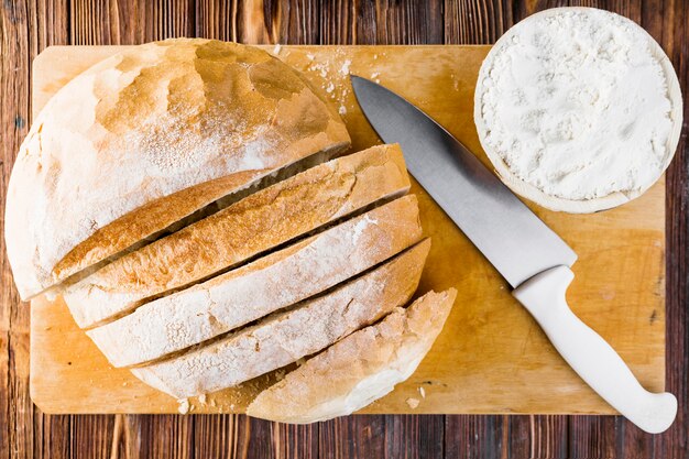 Foto grátis fatias de pão, faca e tigela de farinha na tábua de cortar