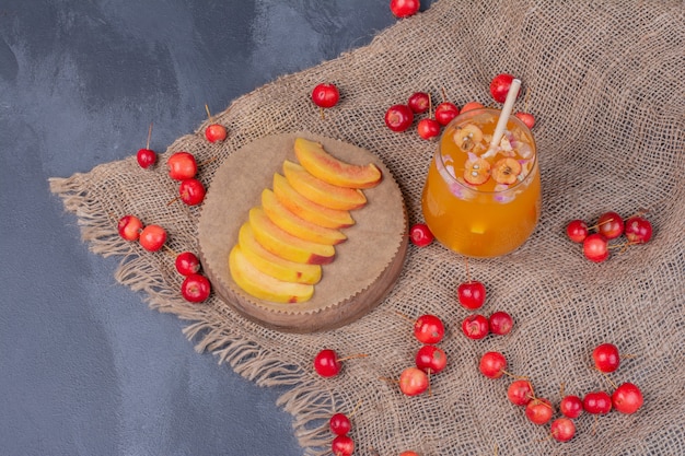 Fatias de pêssego, cerejas e copo de suco de fruta em azul.