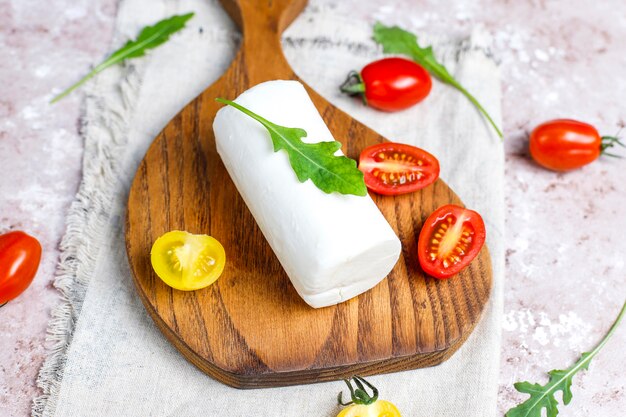 Fatias de queijo de cabra na placa de madeira com ruccola, tomate cereja. Pronto para comer.